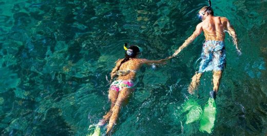 man and woman snorkeling in body of water while holding hands