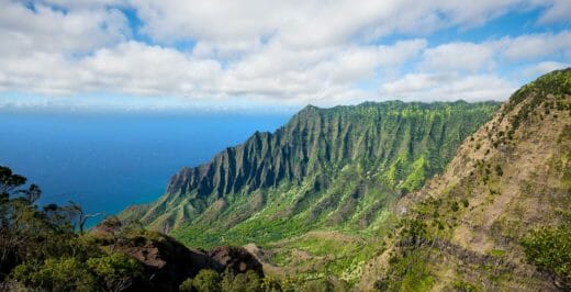 mountain cliff near ocean under white clouds