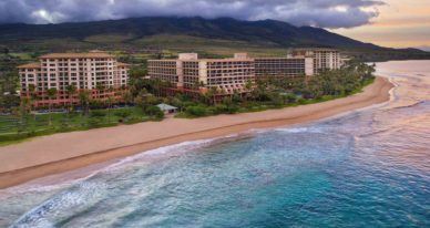 exterior aerial shot of luxury maui beachfront hotel with cloud covered mountain in the background